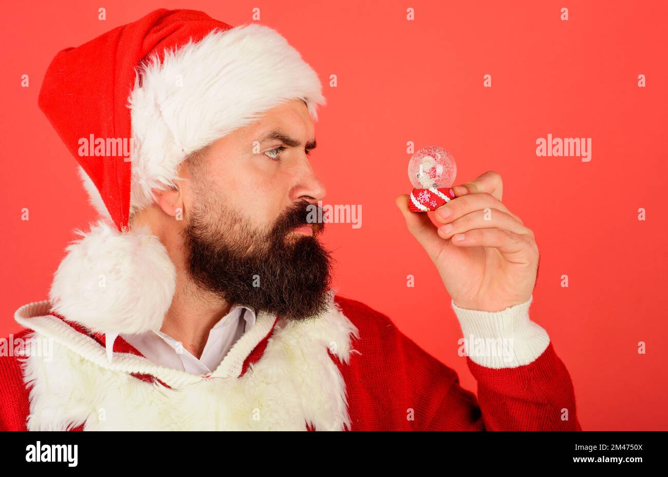 Bärtiger Mann im Weihnachtsmann-Kostüm mit Schneekugel. Weihnachtssnowball. Silvester-Kristallkugel. Stockfoto