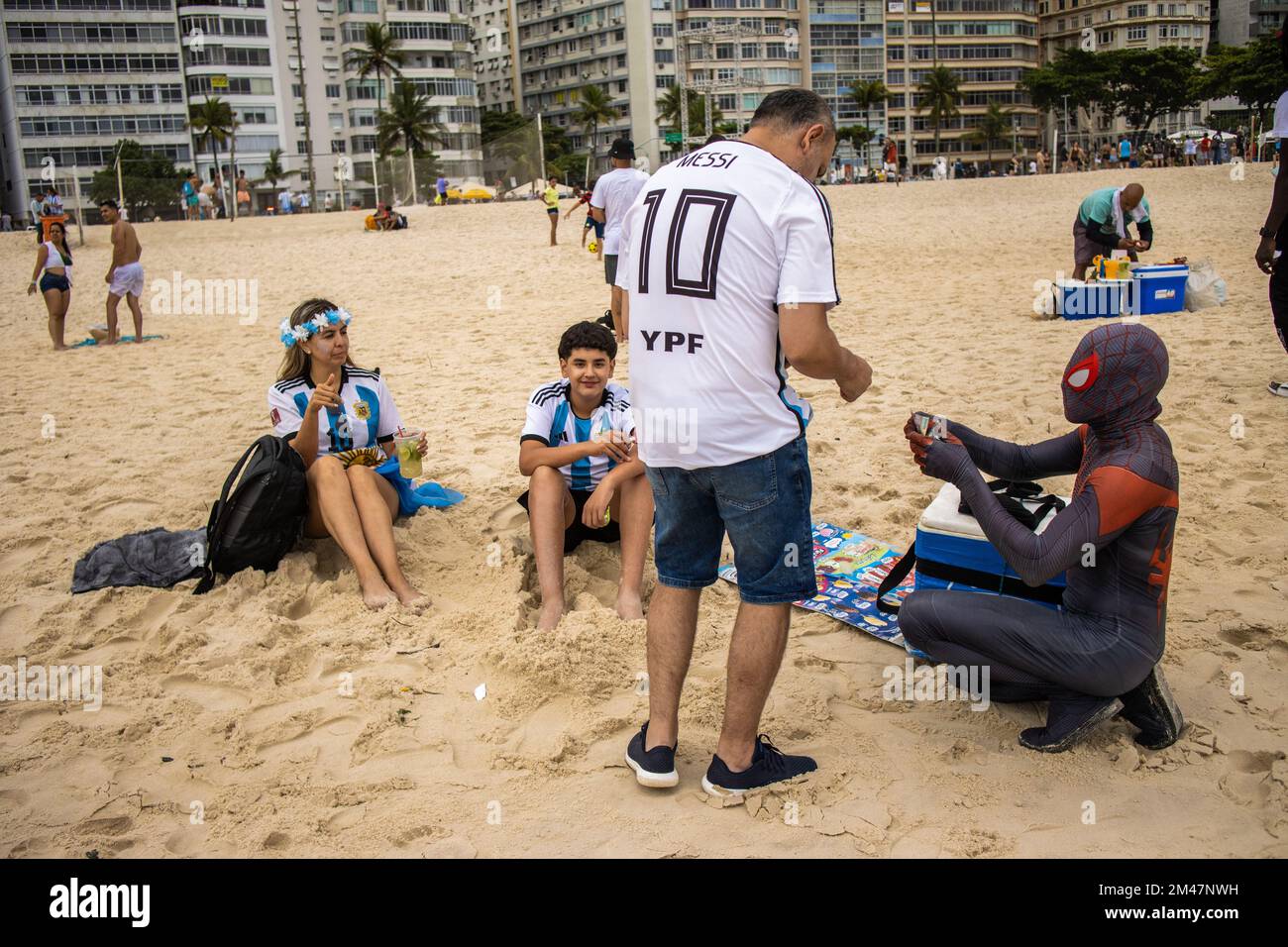 Rio De Janeiro, Brasilien. 18.. Dezember 2022. Eine argentinische Fans-Familie kauft während der Siegesfeier am Copacabana Beach Getränke von einem Straßenverkäufer, der als Spider-man verkleidet ist. Fans der argentinischen Nationalmannschaft versammeln sich in der Bar „Buenos Aires“ am brasilianischen Strand der Copacabana in Rio de Janeiro, um das Endspiel der Katar-Weltmeisterschaft zu sehen. Kredit: SOPA Images Limited/Alamy Live News Stockfoto