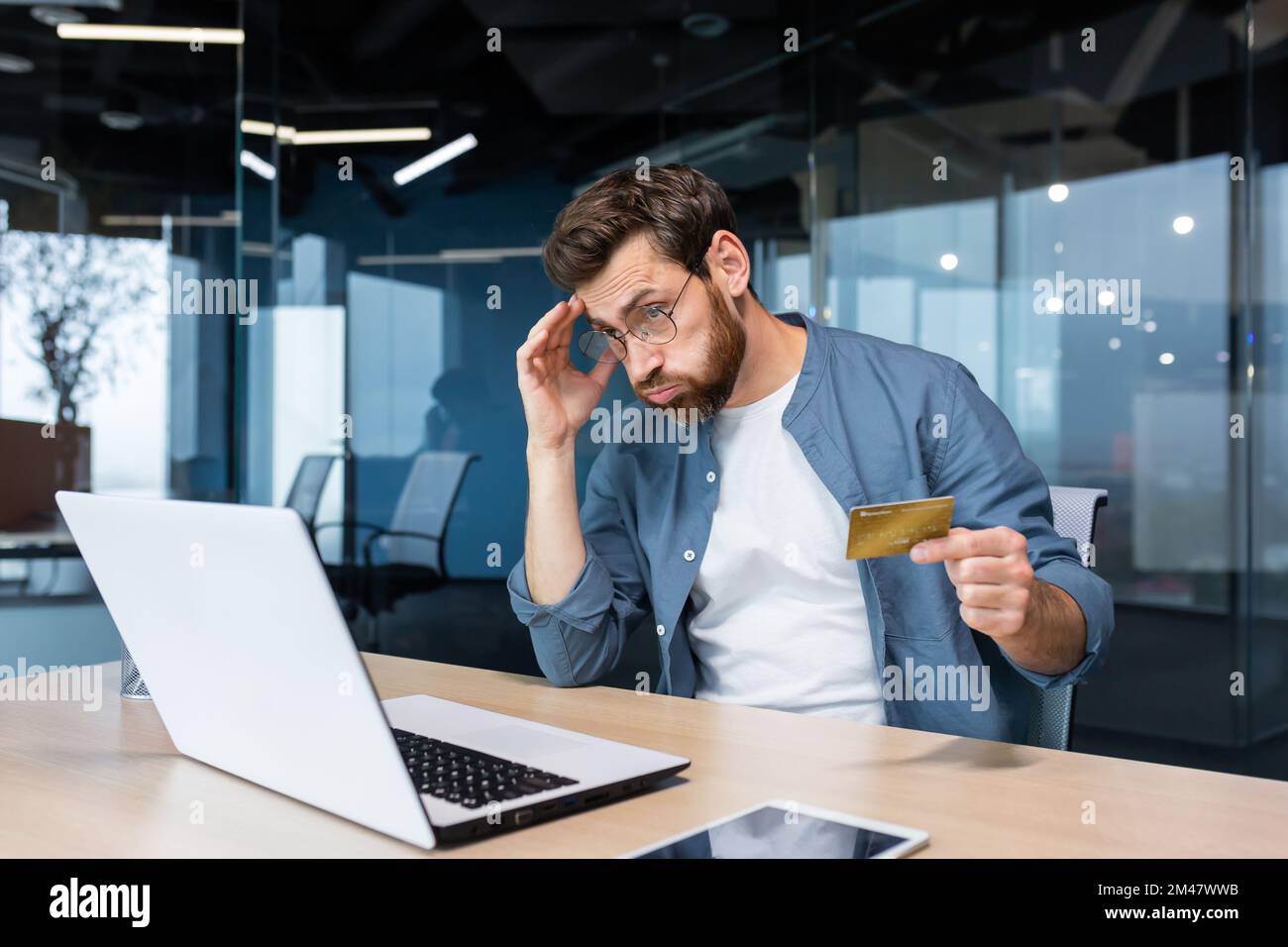 Betrogener und enttäuschter Geschäftsmann, der im Büro arbeitet, Mann mit Bankkreditkarte, der versucht, einen Kauf im Online-Shop zu tätigen, Online-Betrug und -Täuschung. Stockfoto