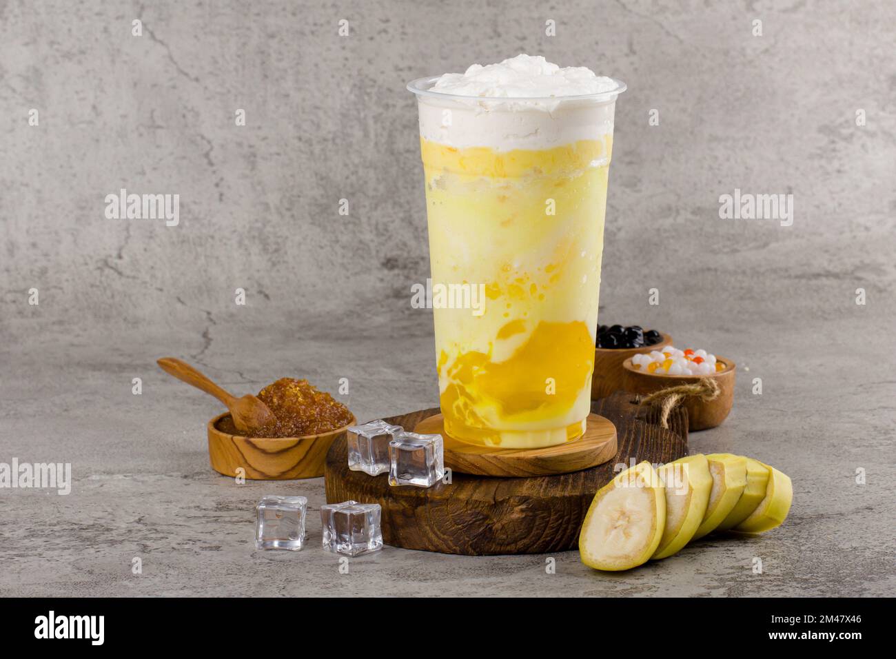 Boba- oder Tapioka-Perlen sind taiwanischer Seifenmilchtee in Plastikbecher mit Bananengeschmack auf texturiertem Hintergrund, Sommererfrischung. Stockfoto