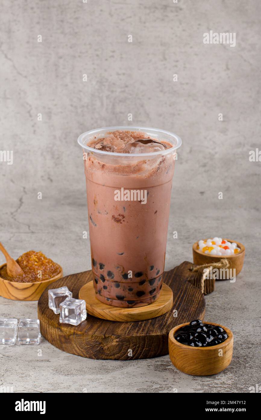 Boba- oder Tapiokapperlen sind taiwanischer Seifenmilchtee in Plastikbecher mit dunklem Schokoladengeschmack auf Texturhintergrund, Sommererfrischung. Stockfoto