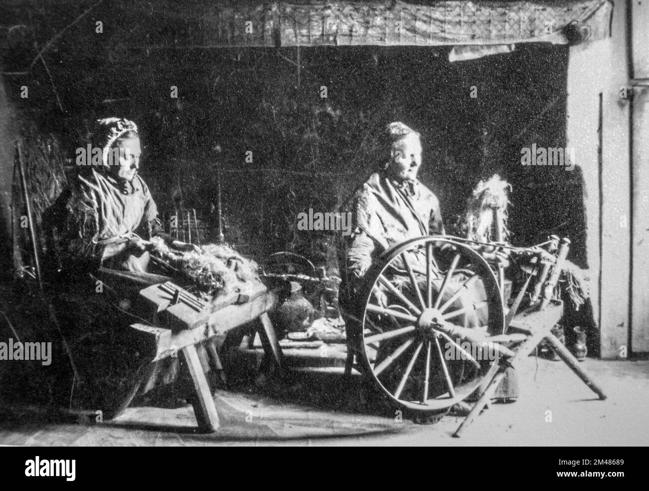 Foto aus dem frühen 20.. Jahrhundert, auf dem zwei alte weibliche Heimspinner gezeigt werden, die mit einem drehenden Holzrad und einem Hacken/Hacken zum Dressen von Flachs arbeiten Stockfoto