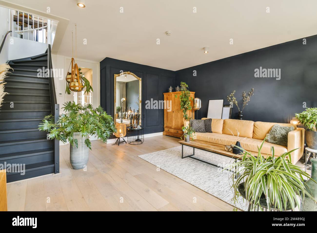 Ein Wohnzimmer mit schwarzen Wänden und Holzfußboden, weißen Verzierungen um die Treppe und Pflanzen in Töpfen auf dem Boden Stockfoto