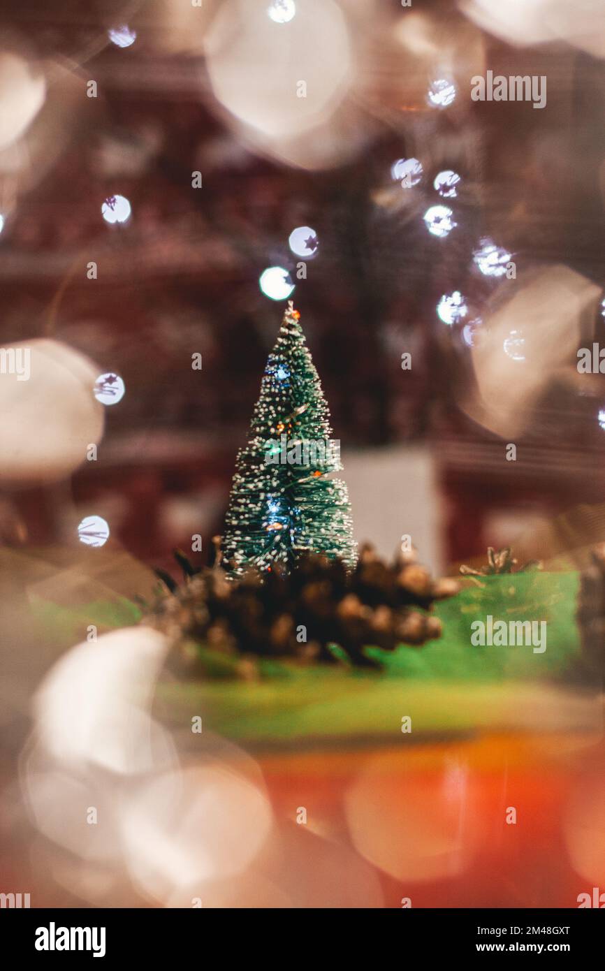 Weihnachtskarte mit Dekoration. Ein grüner künstlicher Weihnachtsbaum mit einem braunen Kegel auf dem Tisch, der von einem abstrakten Licht beleuchtet wird, das dieser Mann erstrahlt Stockfoto