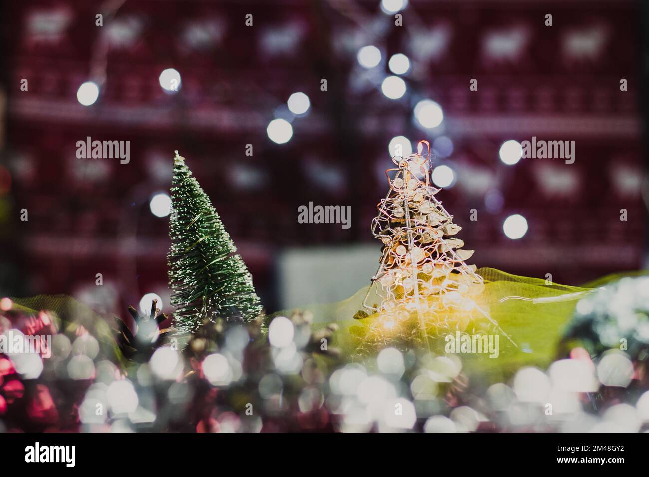 Weihnachts- und Neujahrskarte mit einem kleinen künstlichen grünen Baum und Zapfen auf einem Tisch mit farbenfrohem Hintergrund, in dem die Lichter leuchten und einen Bok erzeugen Stockfoto