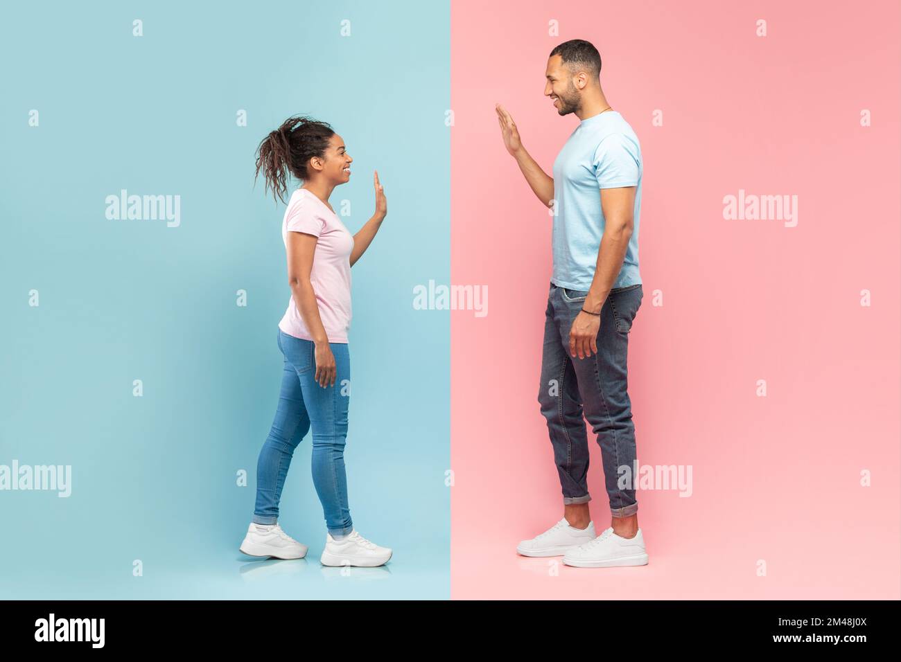 Seitenansicht eines jungen schwarzen Mannes und einer jungen schwarzen Frau, die sich zuwinken, auf einem halbierten pinkfarbenen und blauen Hintergrund Stockfoto