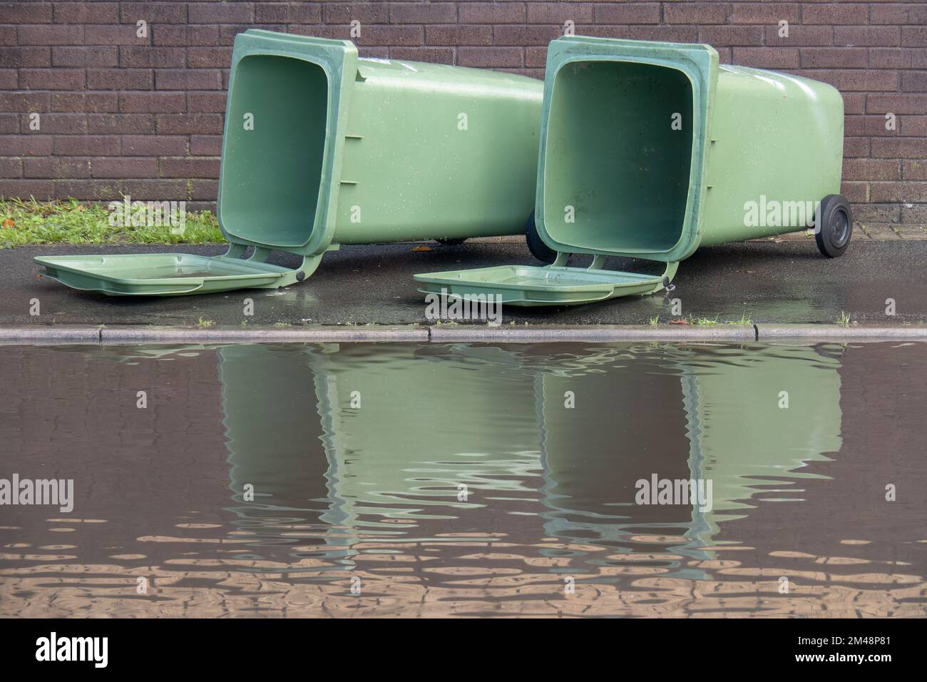 Zwei große grüne Mülltonnen, die auf der britischen Straße liegen, mit großer Pfütze und Überschwemmungen. Nach dem Sturm Stockfoto