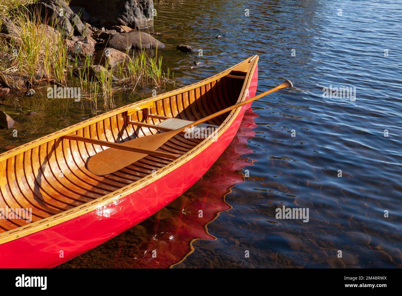 Rotes Holzkanu im Wasser am Ufer eines nördlichen Minnesota Sees Stockfoto