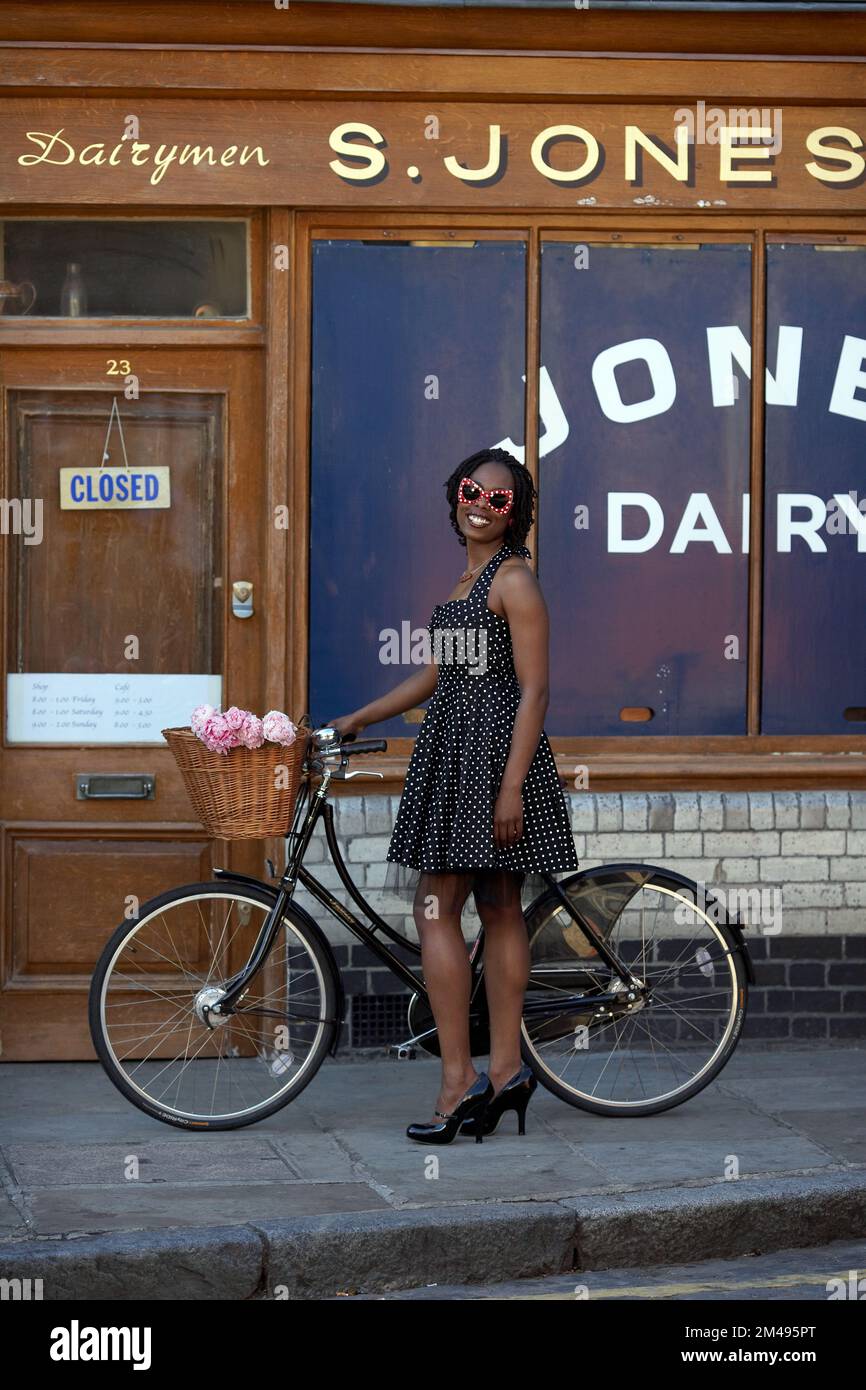 Mädchen steht mit Fahrrad vor dem alten Laden in der Colombia Road, Flower Market, East London, Großbritannien Stockfoto