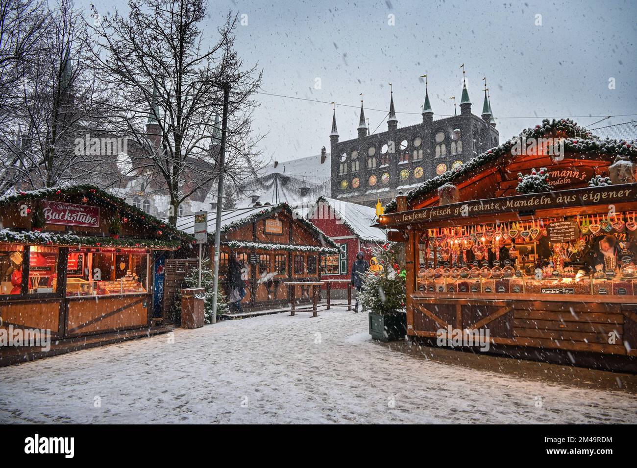 Lübeck, Deutschland, 15. Dezember 2022: Weihnachtsmarkt im Schnee mit romantischen Verkaufsständen und das historische Rathaus von Lübeck im Hintergrund, Copy Spa Stockfoto