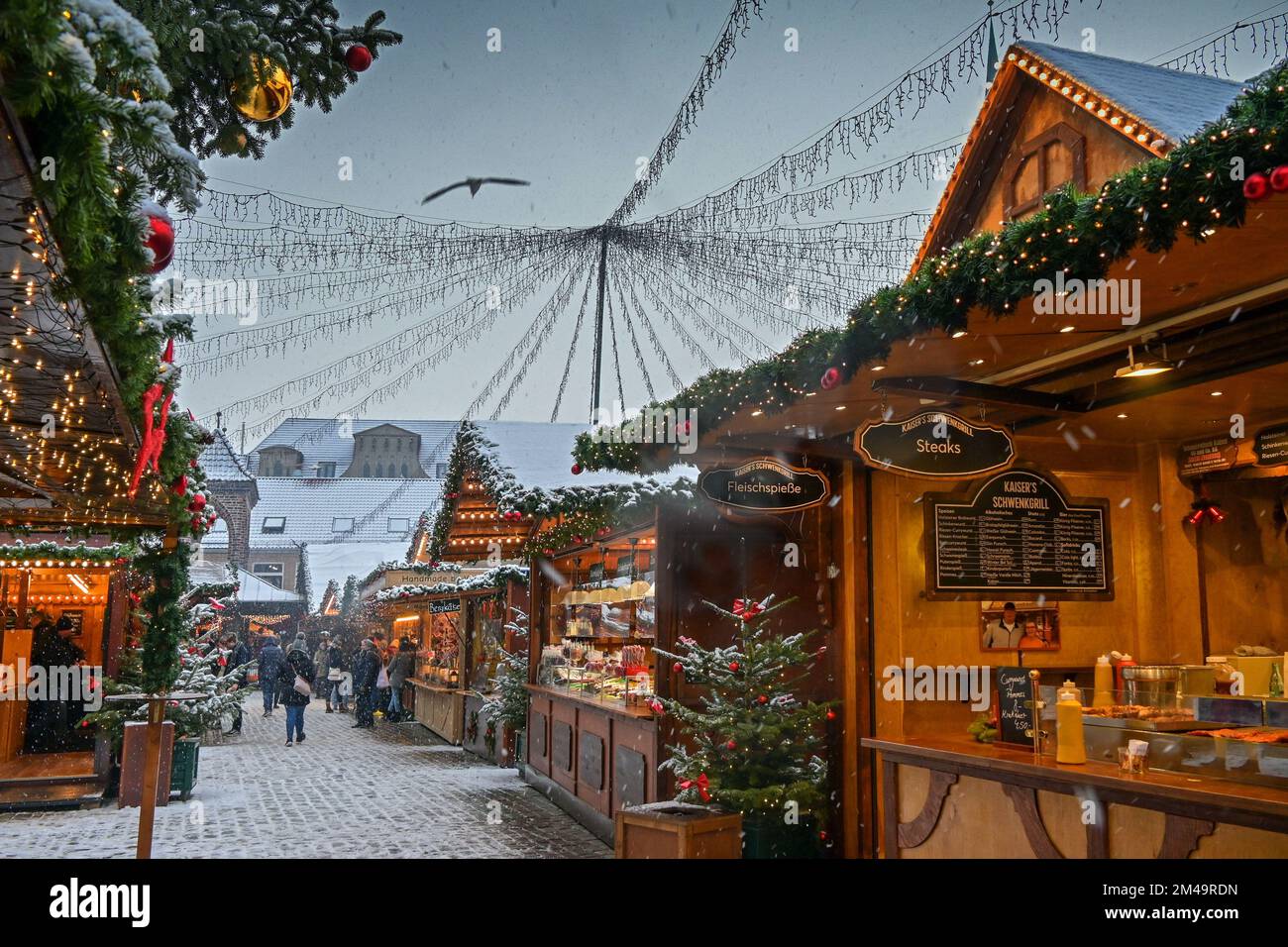 Lübeck, Deutschland, 15. Dezember 2022: Weihnachtsmarkt an einem verschneiten Tag mit romantischen Holzständen und der historischen Altstadt von Lübeck, Kopierraum, selec Stockfoto
