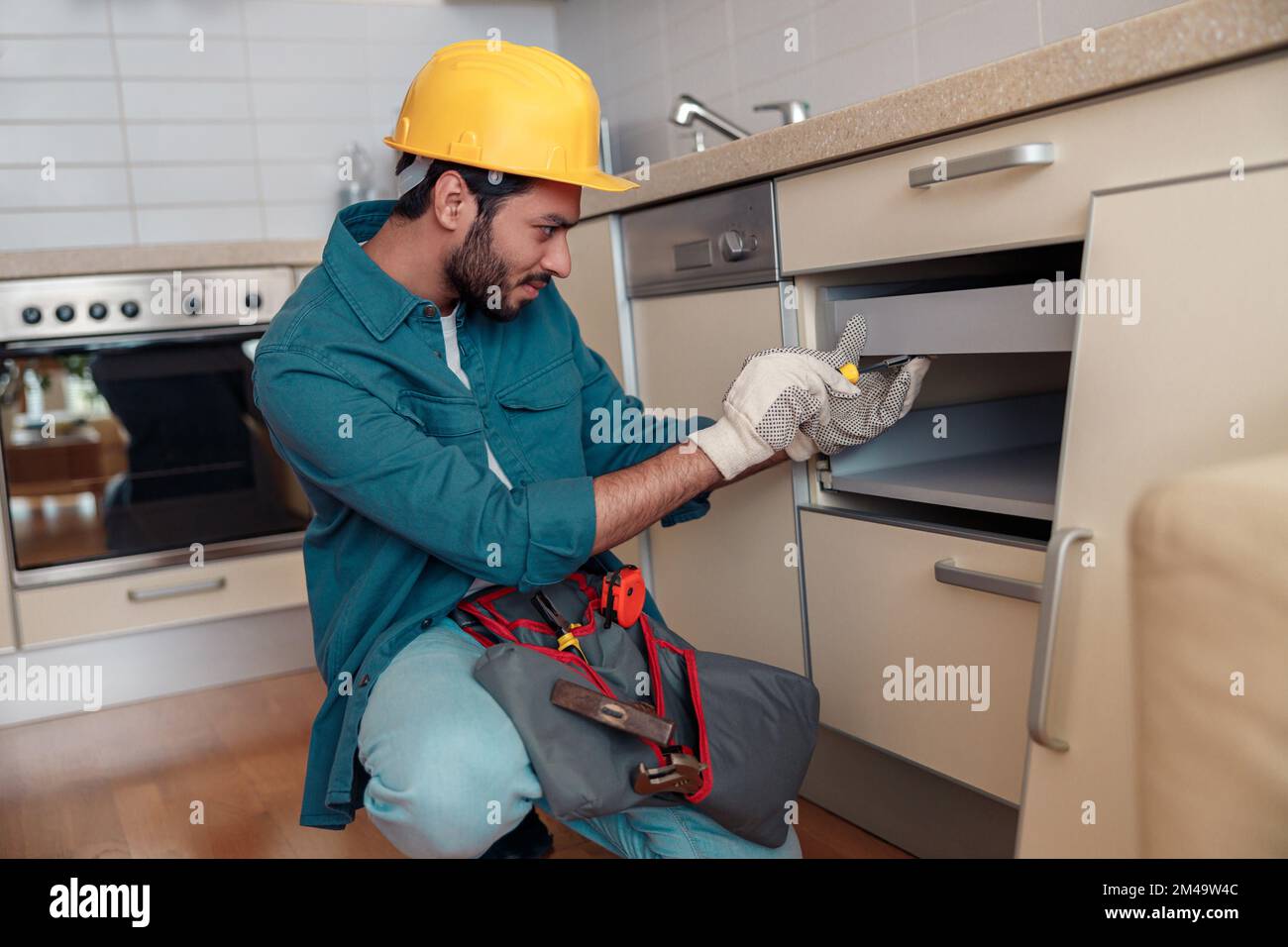 Fokussierter professioneller Arbeiter in Uniform montiert Möbel in der Küche. Reparaturkonzept Stockfoto