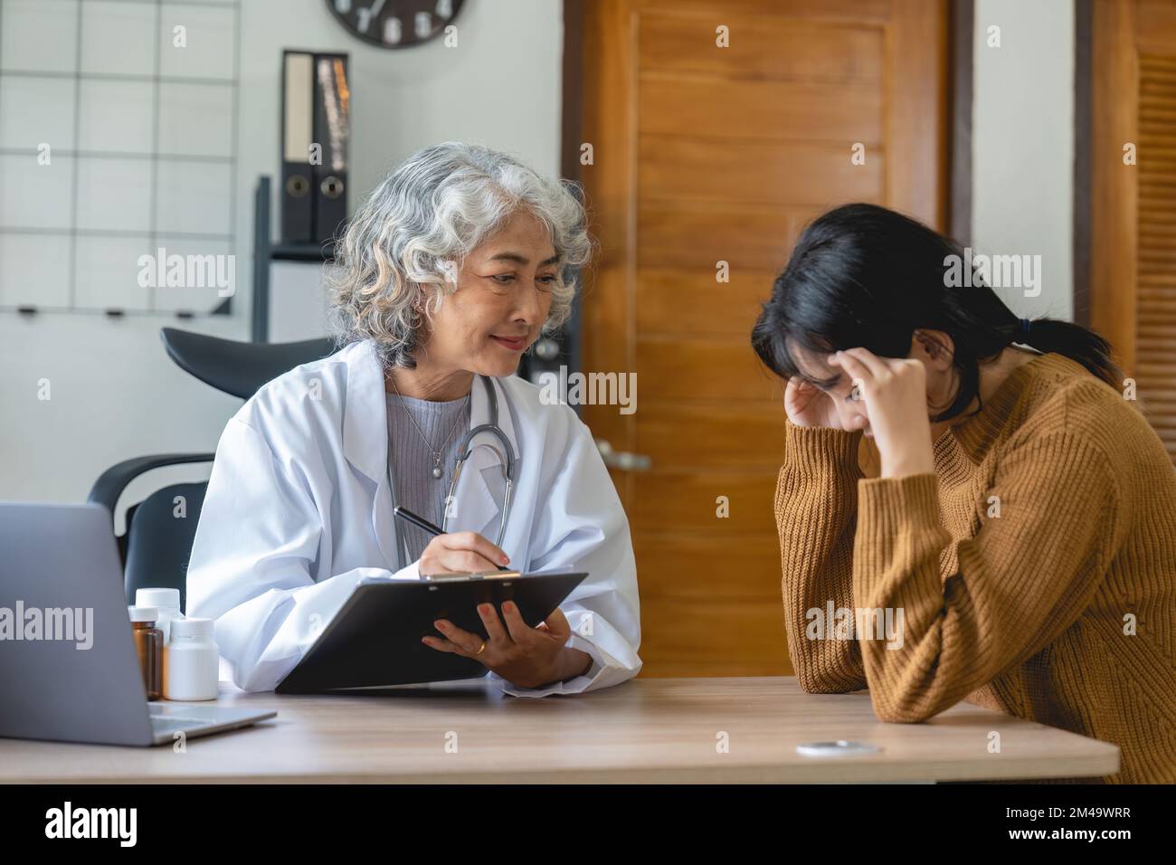 Oberarzt, der einer Frau in ihrer Praxis assistiert. Der Patient weint und fühlt sich hoffnungslos Stockfoto