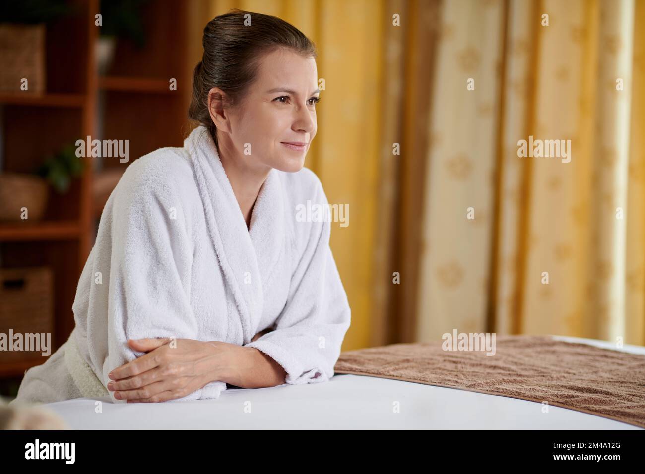 Porträt einer lächelnden erwachsenen Frau im weißen Bademantel, die sich nach Verjüngungseingriffen entspannt Stockfoto