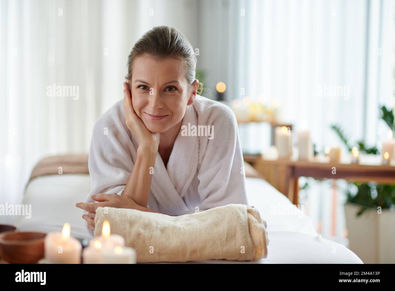 Lächelnde Frau mittleren Alters, die nach einer entspannenden Massage im Bett im Spa-Salon liegt Stockfoto