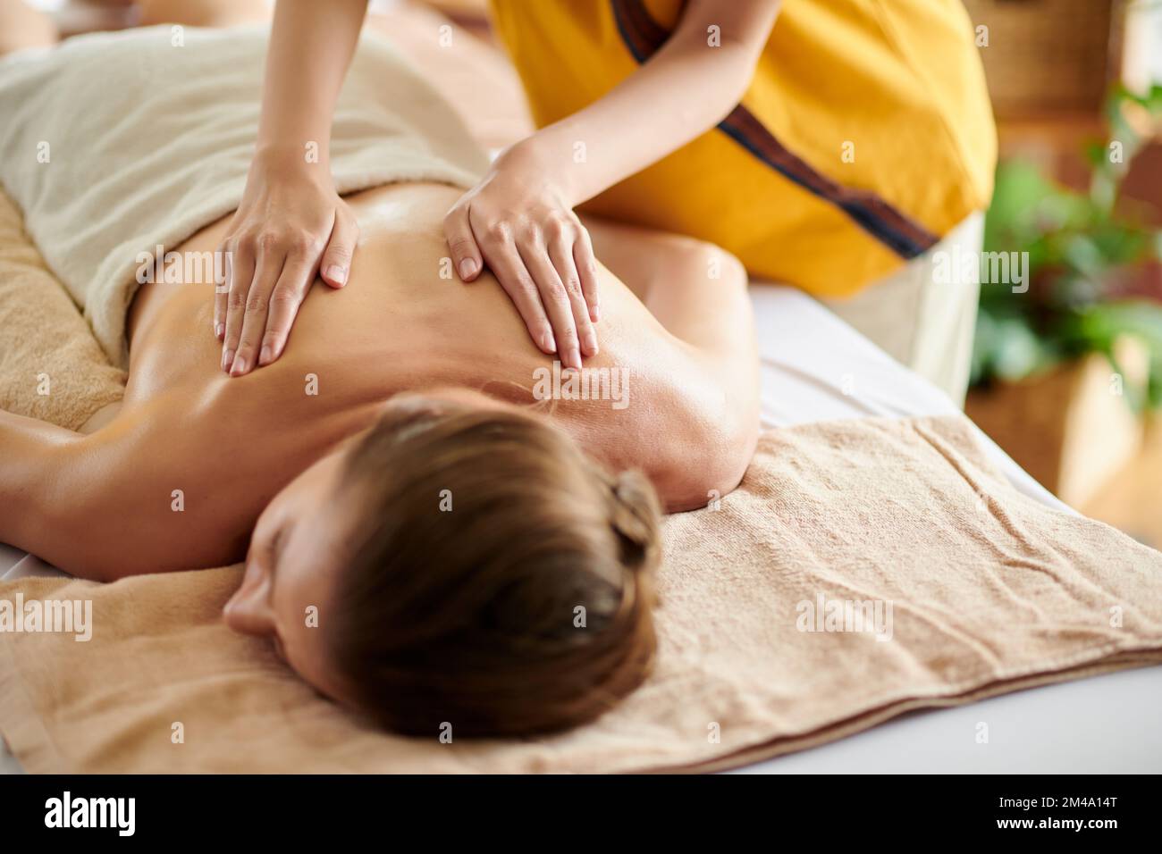 Hände einer Masseurin, die Öl auf den Rücken des Kunden streut Stockfoto