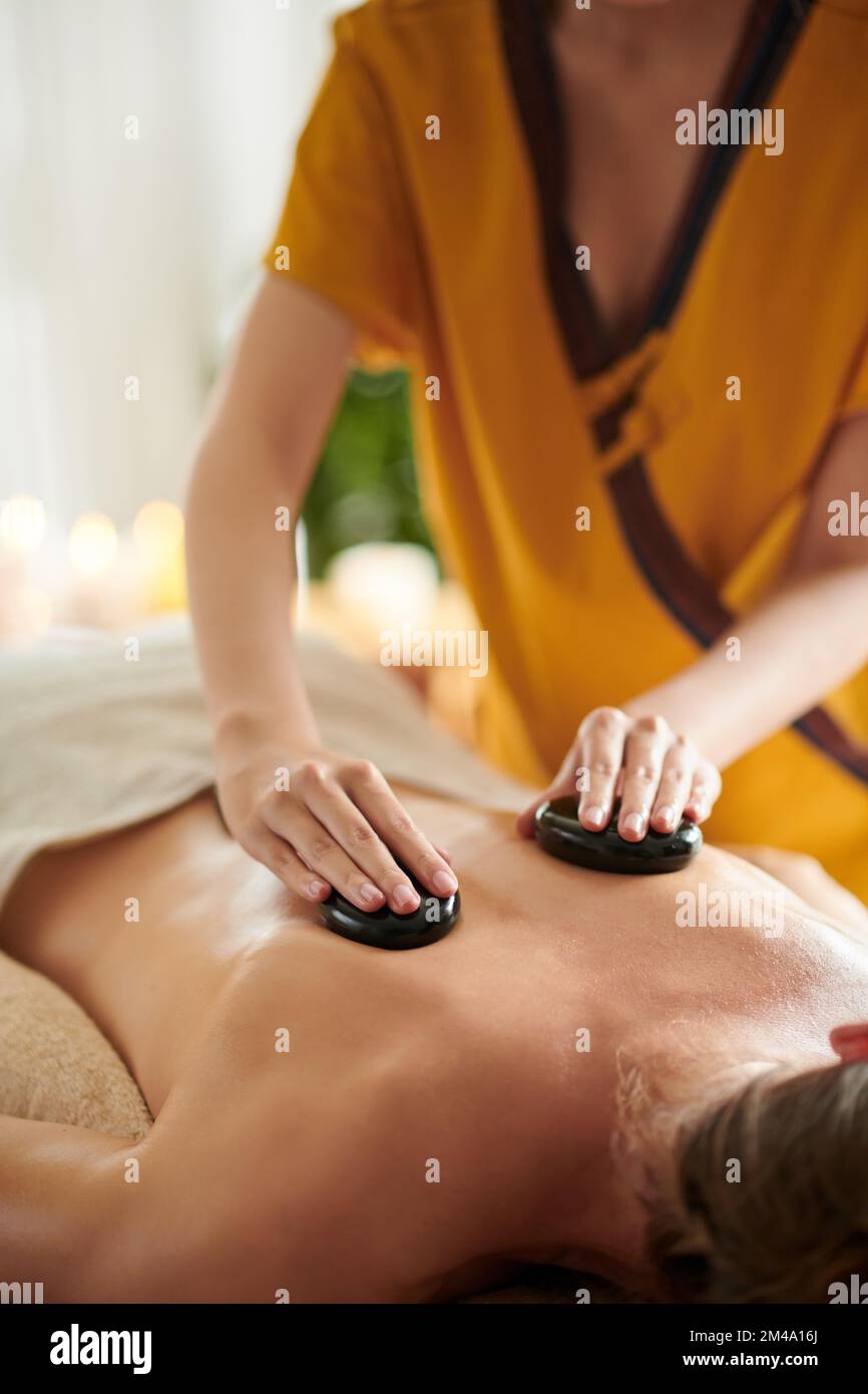 Abgeschnittenes Bild einer Masseurin, die einer Klientin eine entspannende Steinmassage gibt Stockfoto