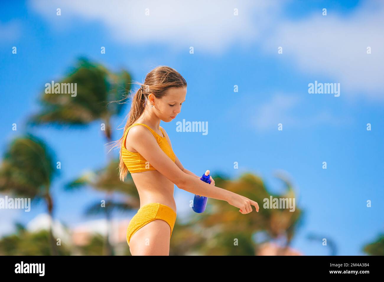 Ein bezauberndes Teenager-Mädchen in gelbem Bikini, das Sonnencreme am Strand aufträgt Stockfoto
