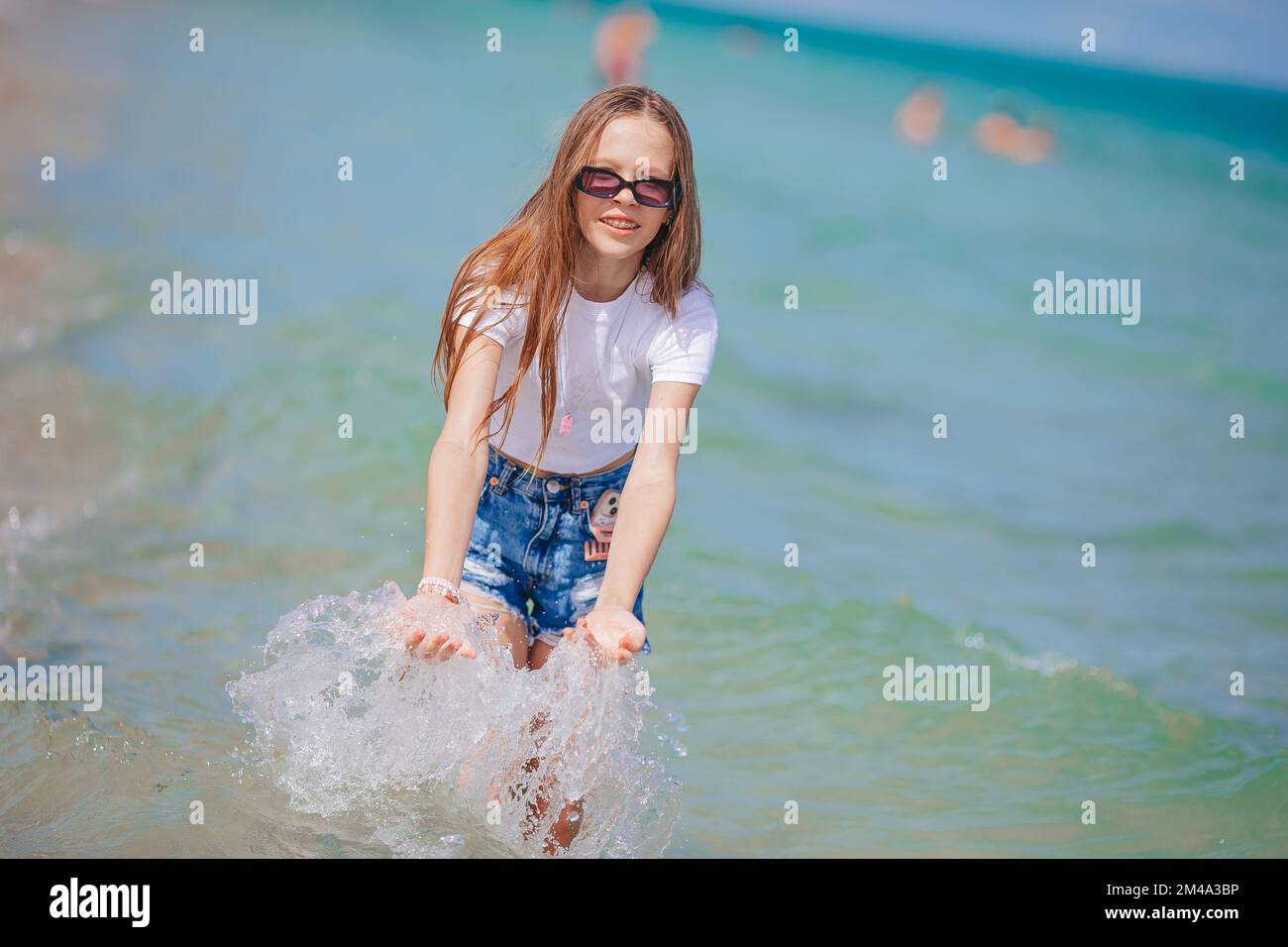 Ein kleines glückliches Mädchen, das in klarem türkisfarbenem Wasser spritzt und läuft Stockfoto