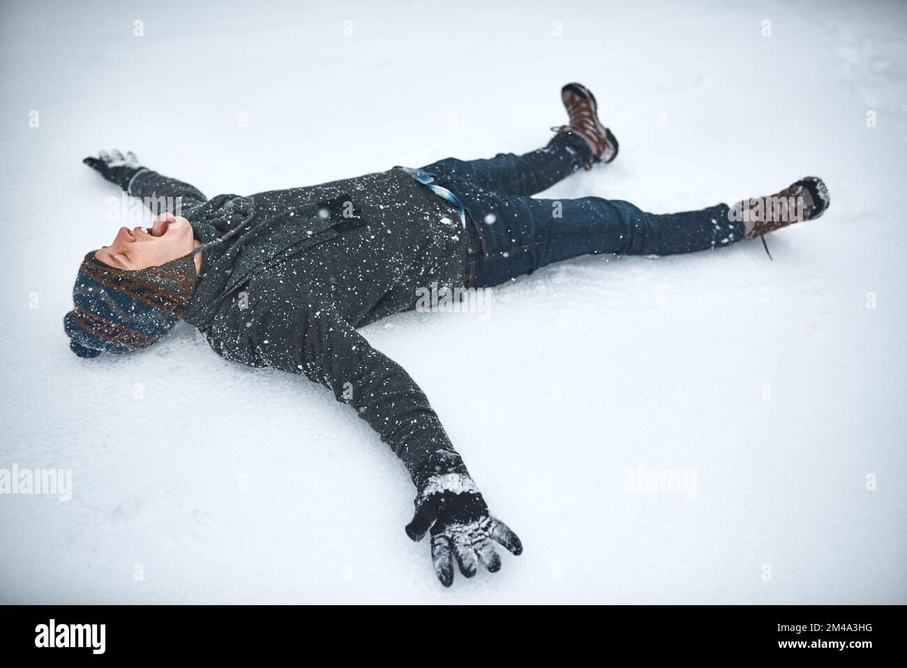 Schnee bringt mich zurück in meine Kindheit. Ein junger Mann, der im Schnee liegt und einen Schneeengel macht. Stockfoto
