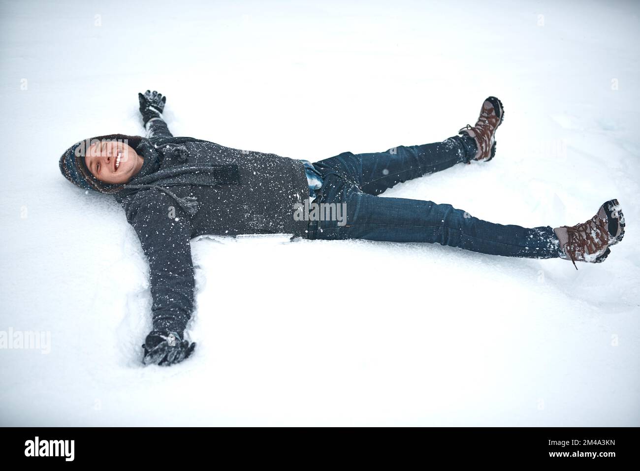 Wenn dir das Leben Schnee gibt, mach Schneeengel. Ein junger Mann, der im Schnee liegt und einen Schneeengel macht. Stockfoto