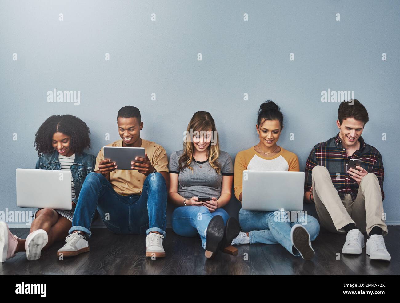 Die technologiebewusste Generation. Studiofoto einer Gruppe junger Menschen, die drahtlose Technologie vor grauem Hintergrund verwenden. Stockfoto
