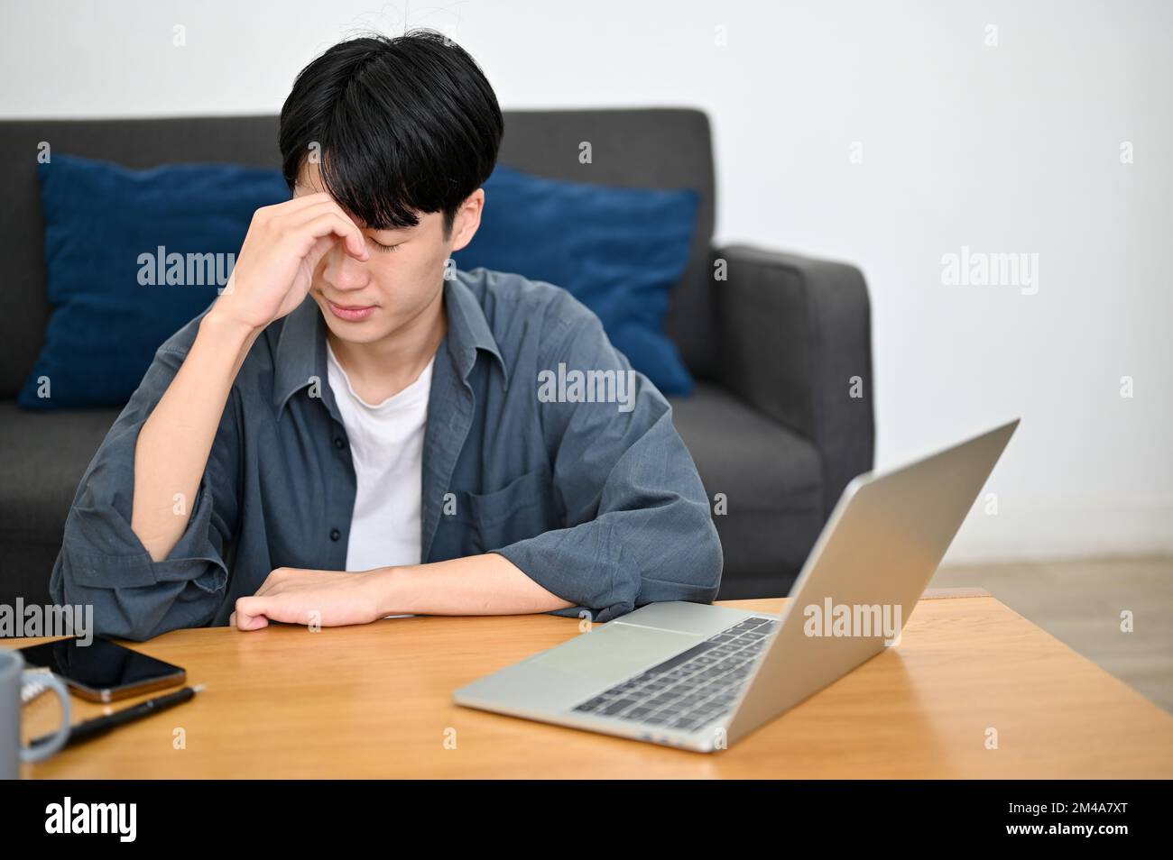 Gestresster und aufmerksamer junger asiatischer Mann sitzt im Wohnzimmer und hat ein Problem mit seinem Projekt, trifft eine schwere Entscheidung, verärgert über seinen Schultest. Stockfoto