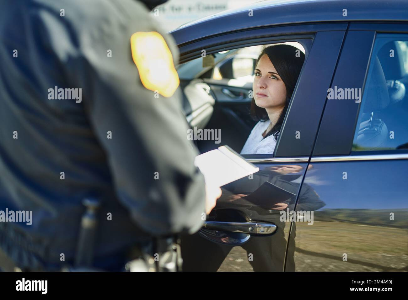 Ich werde dir eine Strafe wegen zu schnellen Fahrens auferlegen müssen. Ein nicht wiedererkennbarer, männlicher Verkehrsoffizier, der einem weiblichen Zivilisten an einer Straßensperre ein Ticket ausstellt. Stockfoto