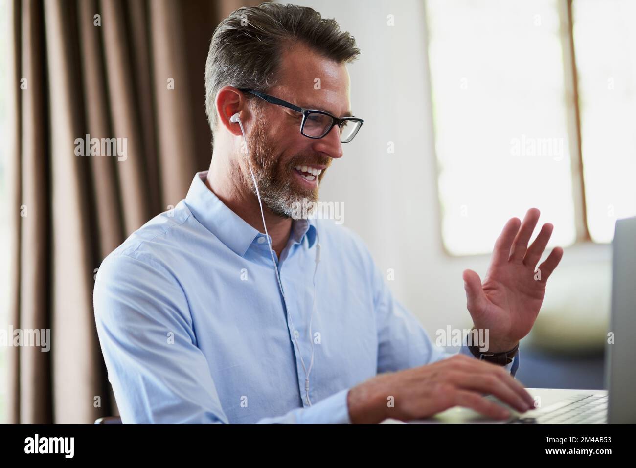 Hallo von dieser Seite der Welt. Ein erwachsener Geschäftsmann winkt, während er von zu Hause aus mit einem Notebook arbeitet. Stockfoto