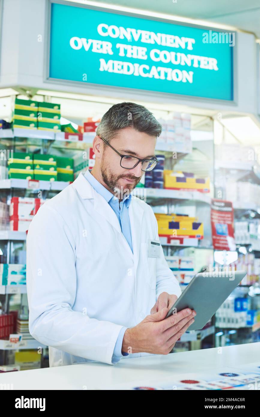 Online-Zusammenarbeit mit anderen medizinischen Fachkräften zur Maximierung von Gesundheitsergebnissen. Ein reifer Apotheker, der eine digitale Tablette in einer Apotheke verwendet. Stockfoto