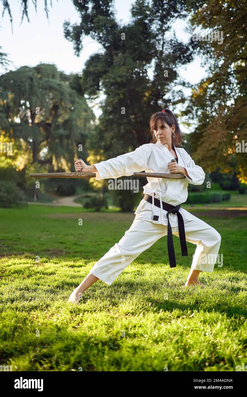 Karate-Kämpferin in weißem Kimono und schwarzem Gürtel, die im Freien Karate in der Natur praktiziert. Sport- und Kampfsportkonzept. Stockfoto