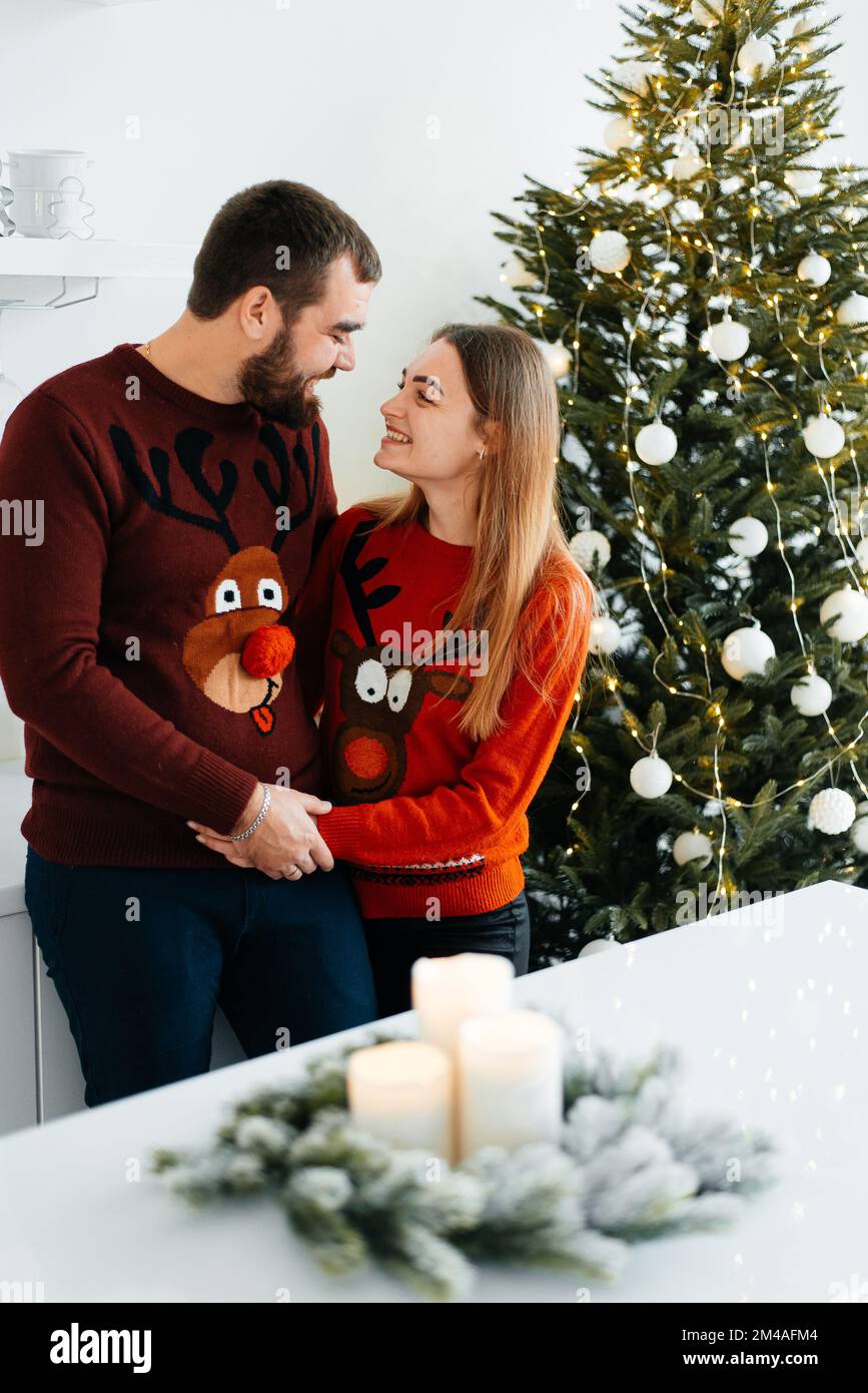Ein verliebtes Paar umarmt und küsst sich in der Nähe des Weihnachtsbaums im dekorierten Inneren des Weihnachtsbaums zu Hause an einem Weihnachtsurlaub im Winter. Ein Mann Stockfoto