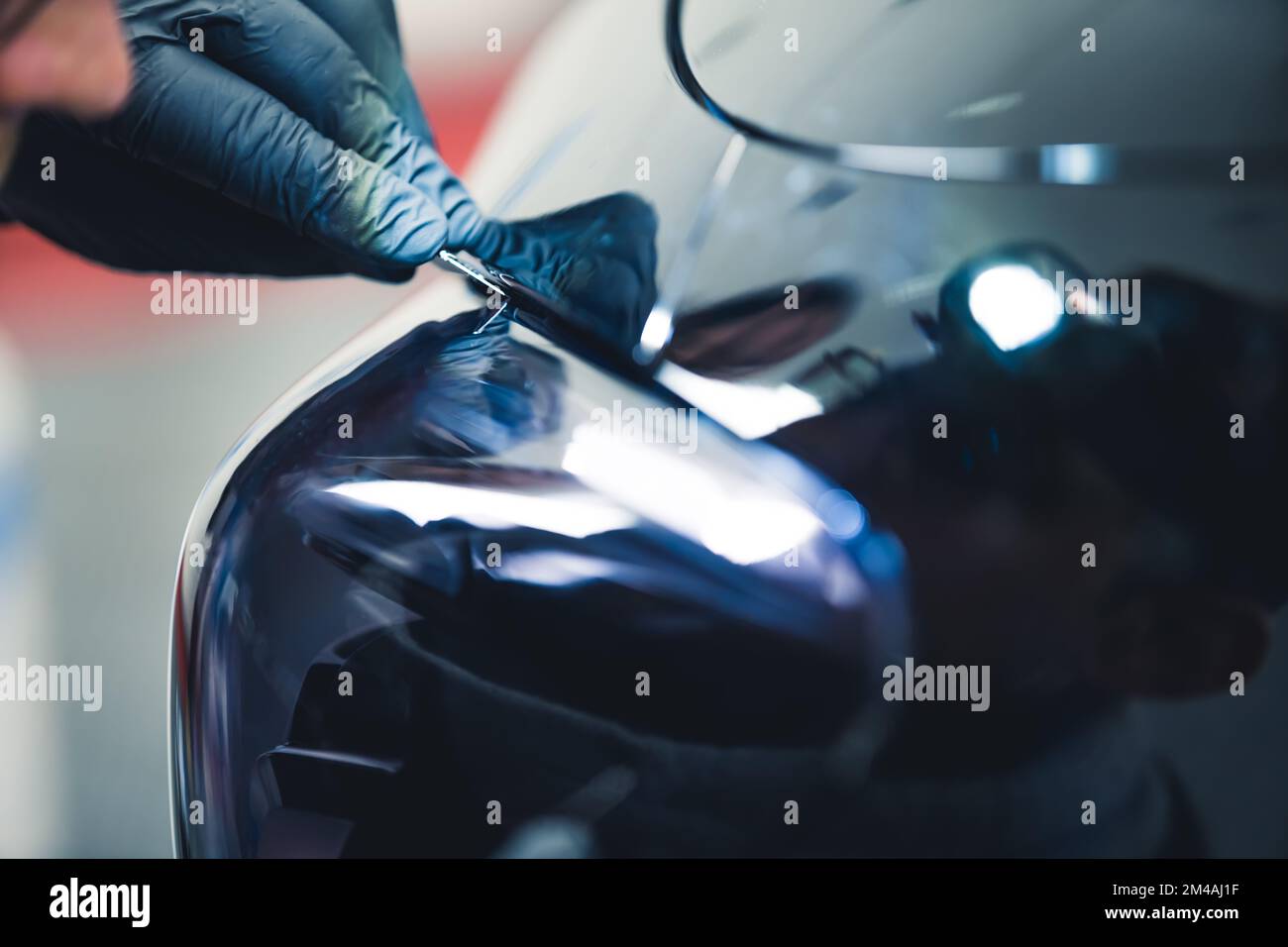 Nahaufnahme einer Person mit blauen Handschuhen, die sich hineinlehnt, um am Rücklicht eines schwarzen Autos in einer Garage zu arbeiten. Autoteile. Horizontale Indoor-Aufnahme. Hochwertiges Foto Stockfoto