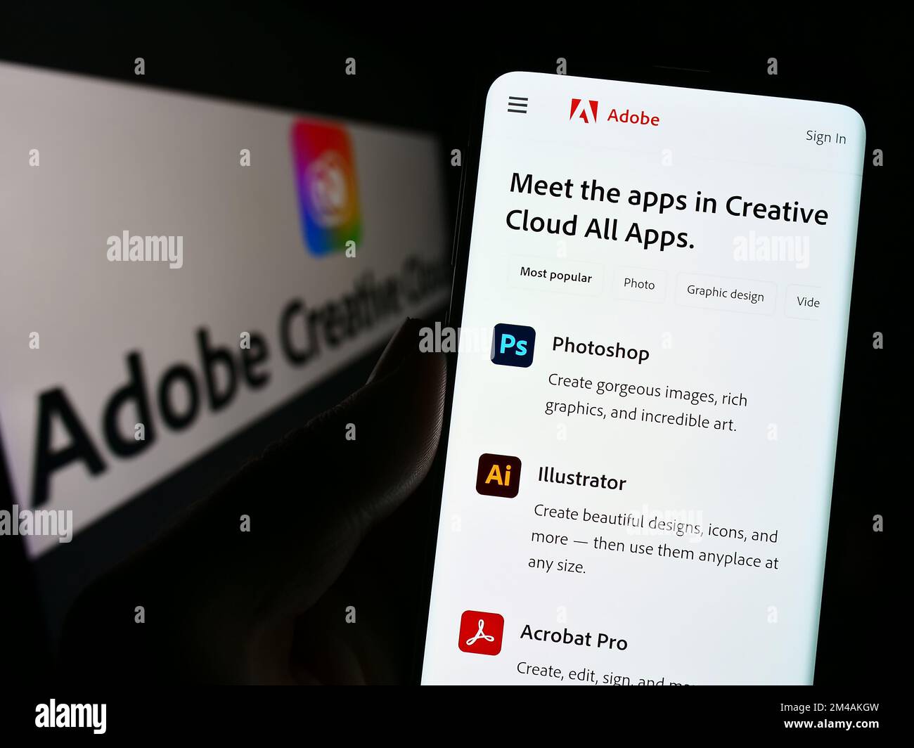 Person, die ein Mobiltelefon mit einer Webseite der Software Adobe Creative Cloud auf dem Bildschirm vor dem Firmenlogo hält. Konzentrieren Sie sich auf die Mitte des Telefondisplays. Stockfoto