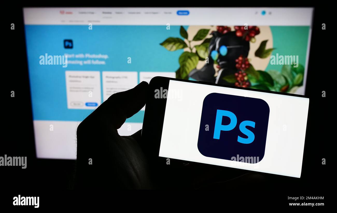 Person, die ein Smartphone mit dem Logo der Grafik-Editor-Software Adobe Photoshop auf dem Bildschirm vor der Website hält. Konzentrieren Sie sich auf das Display des Telefons. Stockfoto