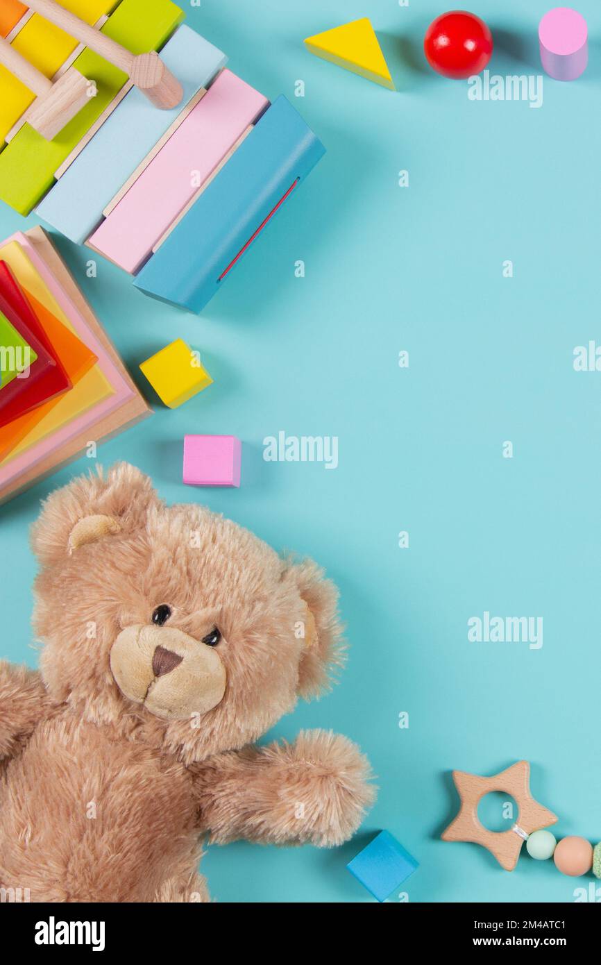 Lernspielzeug für Babys und Kinder – Hintergrund. Teddybär, pädagogisches Spielzeug aus Holz und bunte Bausteine auf hellblauem Hintergrund. Draufsicht, flach liegend Stockfoto