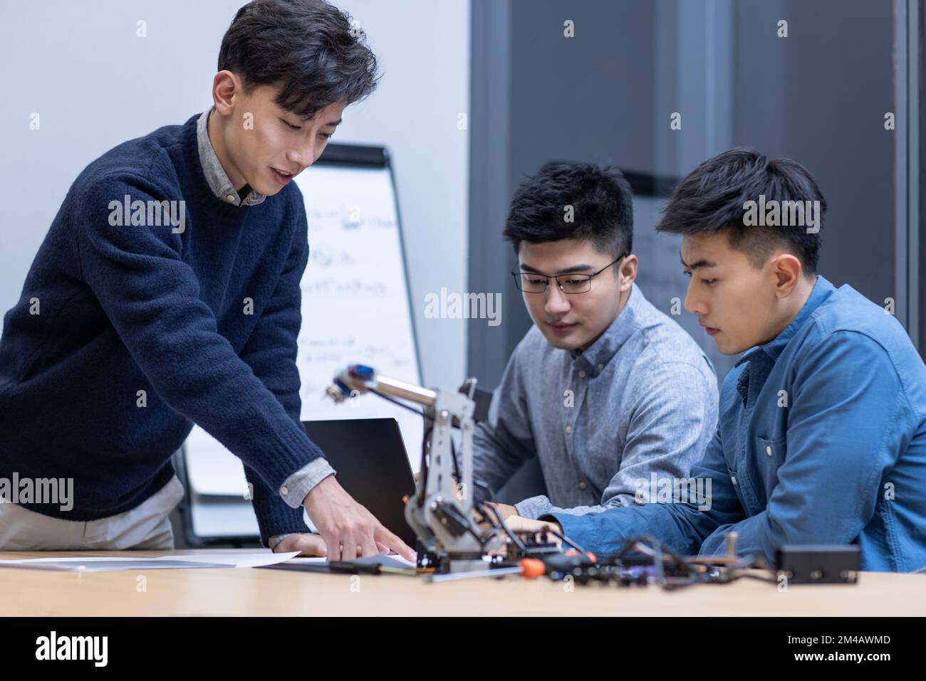 Selbstbewusste chinesische Konstrukteure überprüfen einen Roboterarm Stockfoto