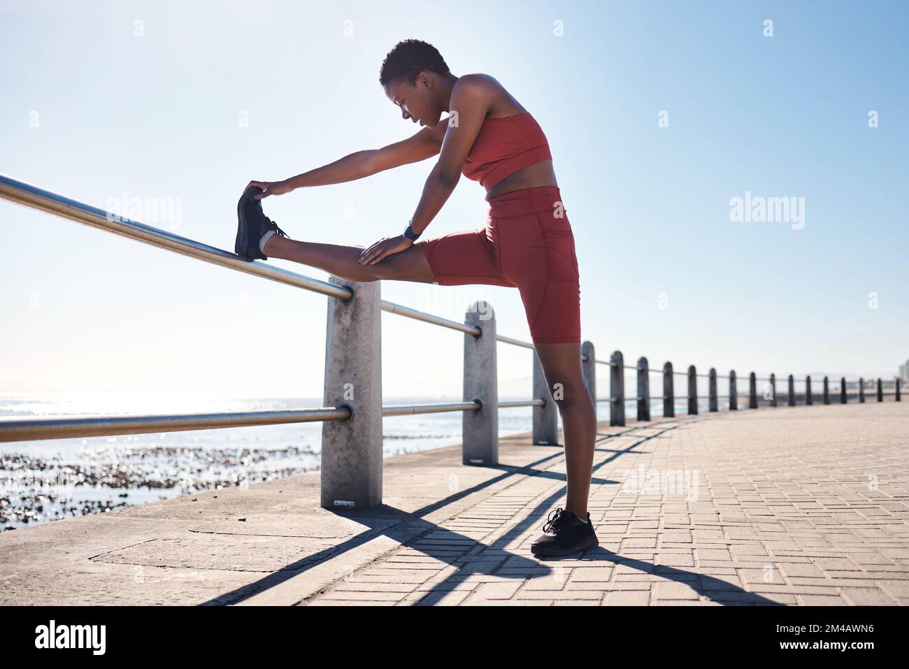 Schwarze Frau, Beine oder Fitness, die sich am Strand, Meer oder Meer für Muskelschmerzen, Gesundheit Wellness oder Marathon bereit macht. Läufer, Sportler Stockfoto