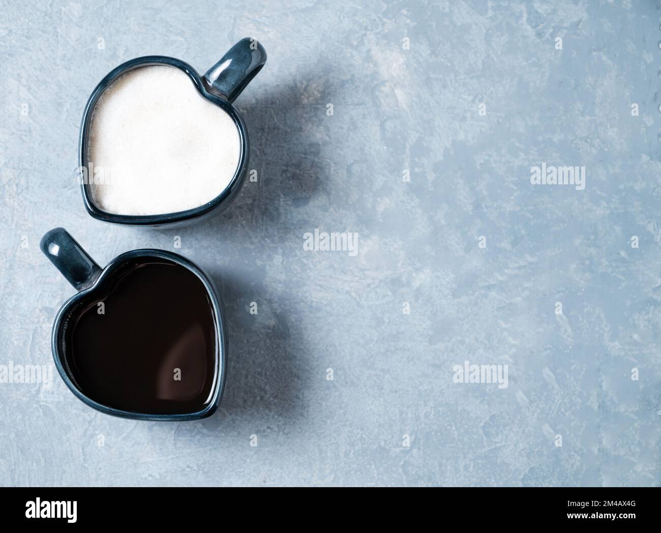 Zwei Tassen in Herzform mit frisch gebrühtem aromatischem Kaffee mit Milch und Espresso auf blauem Hintergrund. Das Konzept der gegensätzlichen Getränke. Draufsicht Stockfoto