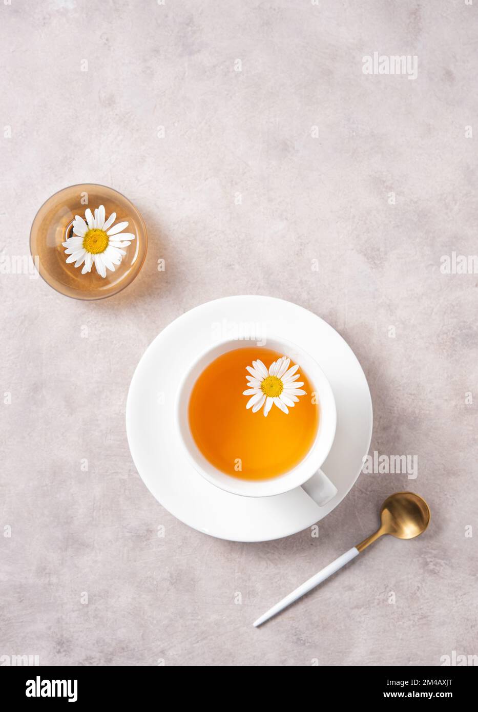 Kamillentee in einem weißen Becher mit Blumen und einer Vase auf pinkgrauem Hintergrund. Ansicht von oben und Bild des Bereichs kopieren Stockfoto