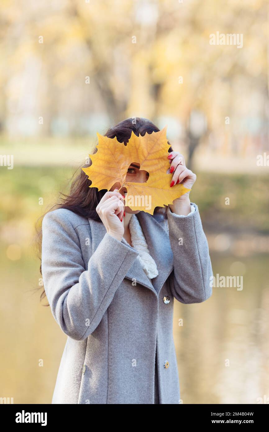 Porträt einer jungen Frau mit langen Haaren, die an einem sonnigen Herbsttag frische Luft atmet und einen grauen Mantel und einen lila Schal trägt. Hochwertiges Foto Stockfoto