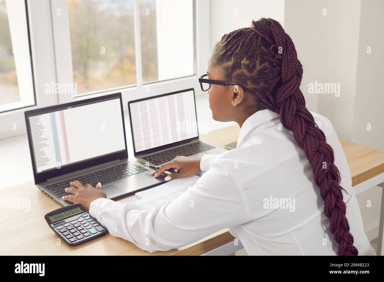 Afroamerikanische Buchhalterin, die im Büro arbeitet, an ihrem Schreibtisch sitzt und Laptops verwendet Stockfoto