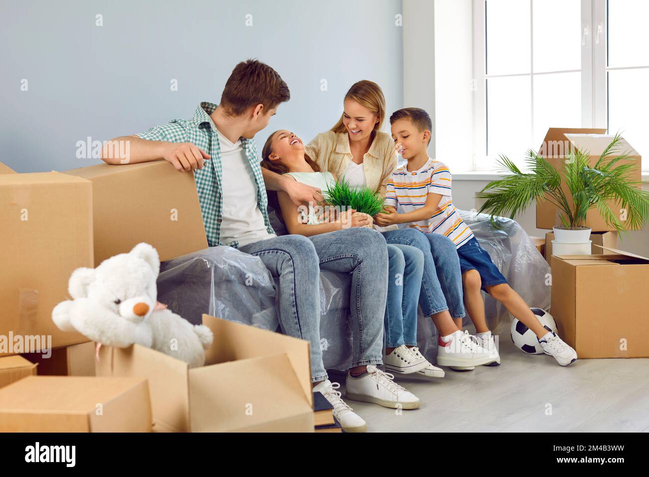 Müde, glückliche Familie mit zwei Kindern, die sich auf dem Sofa zwischen Boxen ruhten, während sie in ein neues Haus zogen. Stockfoto