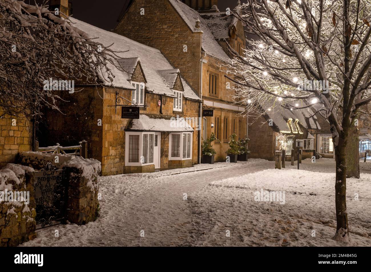Broadway-Dorf und Weihnachtsbäume mit hellen Dekorationen bei Nacht im Schnee. Broadway, Cotswolds, Worcestershire, England Stockfoto