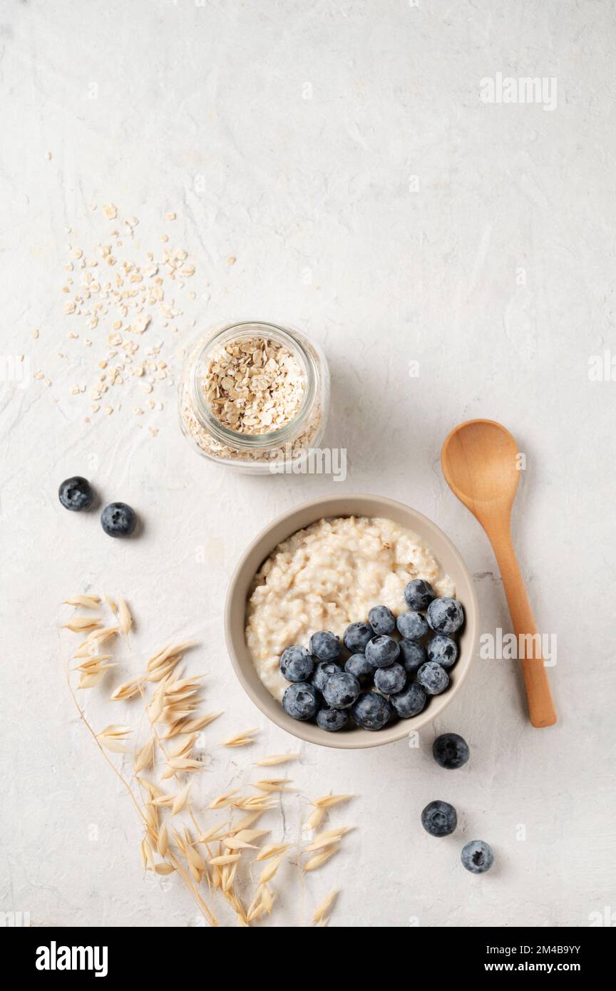 Haferbrei mit Blaubeeren in Schüssel mit Holzlöffel und Glas Haferflocken auf grauem Hintergrund. Das Konzept eines köstlichen, nahrhaften und Stockfoto