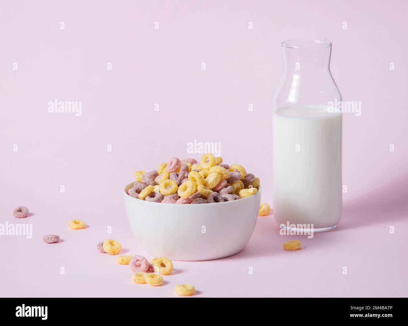 Süße bunte Cornflakes-Ringe in einer weißen Schüssel mit einer Flasche Milch auf pinkfarbenem Hintergrund. Vorderansicht und Bild im Kopierbereich Stockfoto