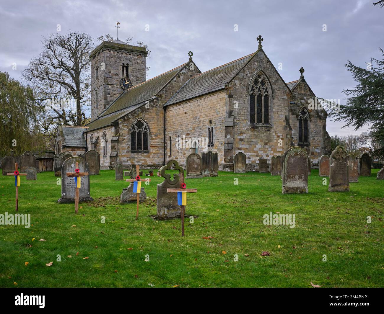 Herbstblick auf die viktorianische, sächsische All Saints Church mit Friedhof und Grabsteinen. Hovingham Stockfoto