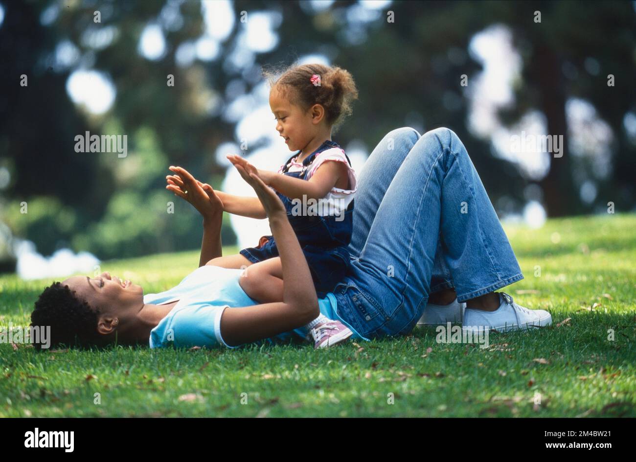 Afroamerikanische Mutter und kleines Mädchen, die im Gras spielen Stockfoto