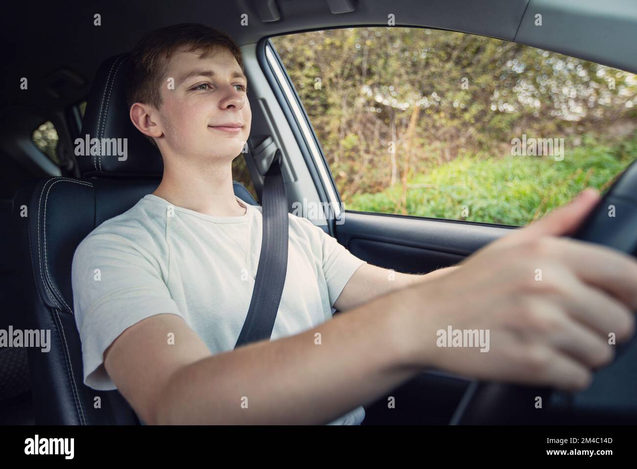 Stolzer und fröhlicher junger Fahrer vor dem Lenkrad, der sein neues Auto selbstbewusst fährt Stockfoto