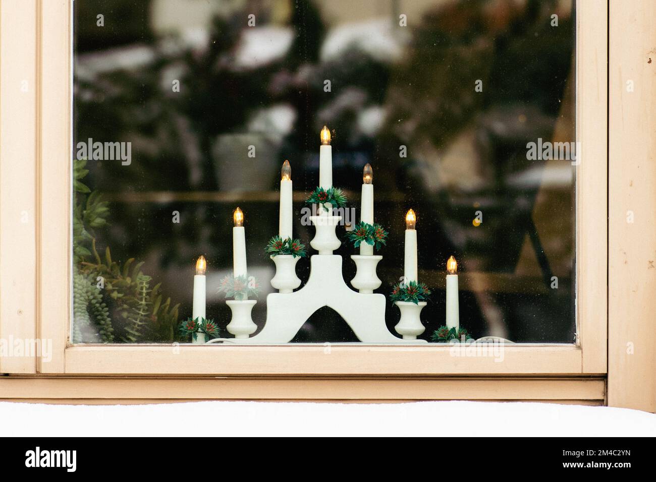 Traditionelle schwedische weihnachtliche Kerzenleuchtbrücke an einem Holzfenster mit Schnee auf der Fensterbank Stockfoto